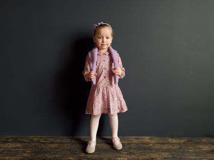 Young girl in a floral dress holding a pink backpack against a dark background