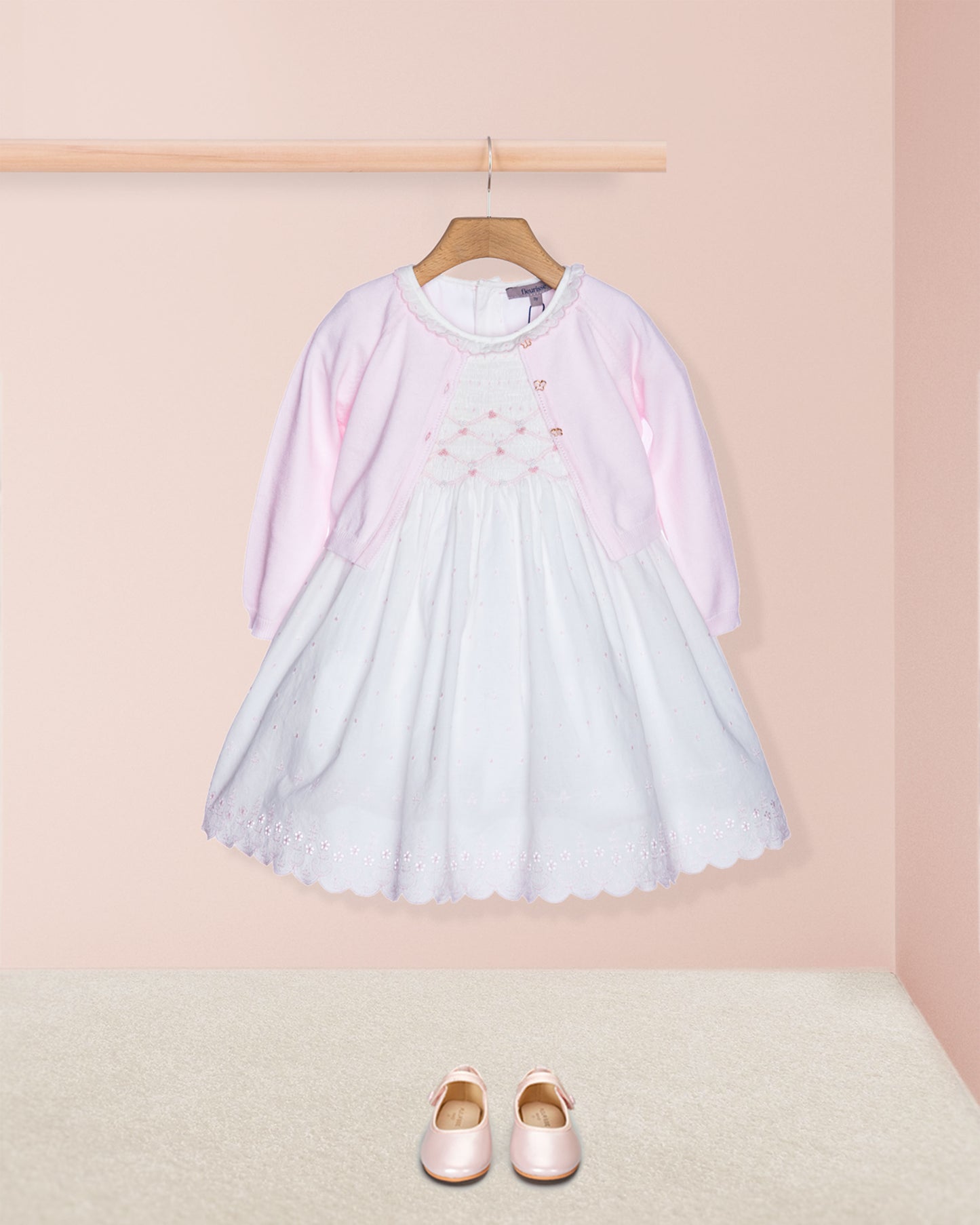 Light blue dress with pink sleeves on a hanger against a pink wall, with matching shoes on the floor.