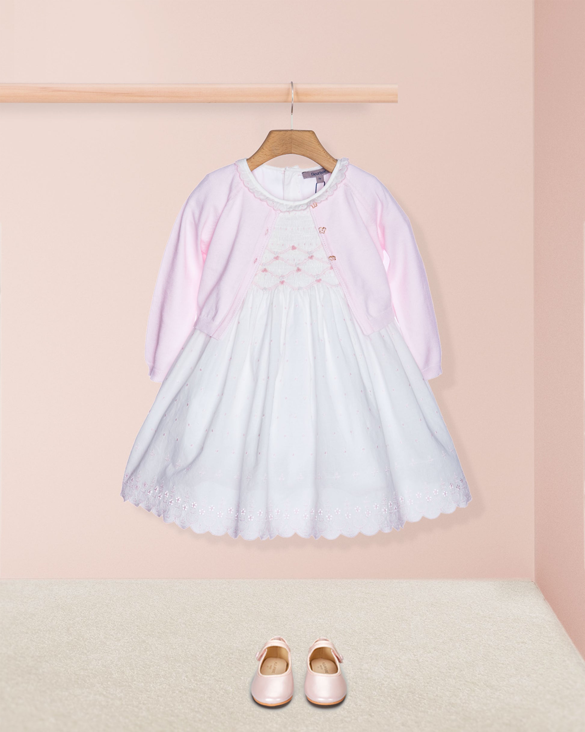 Light blue dress with pink sleeves on a hanger against a pink wall, with matching shoes on the floor.