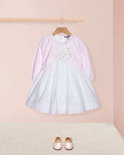 Light blue dress with pink sleeves on a hanger against a pink wall, with matching shoes on the floor.