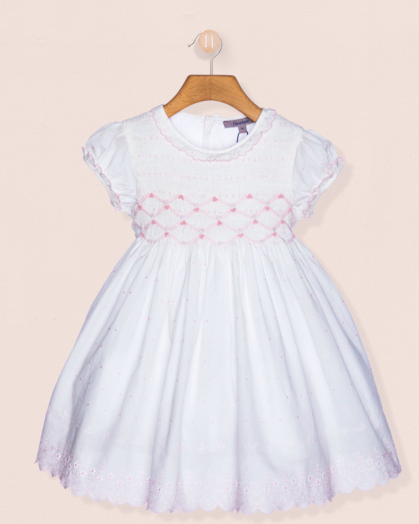 White dress with pink floral embroidery on a beige background
