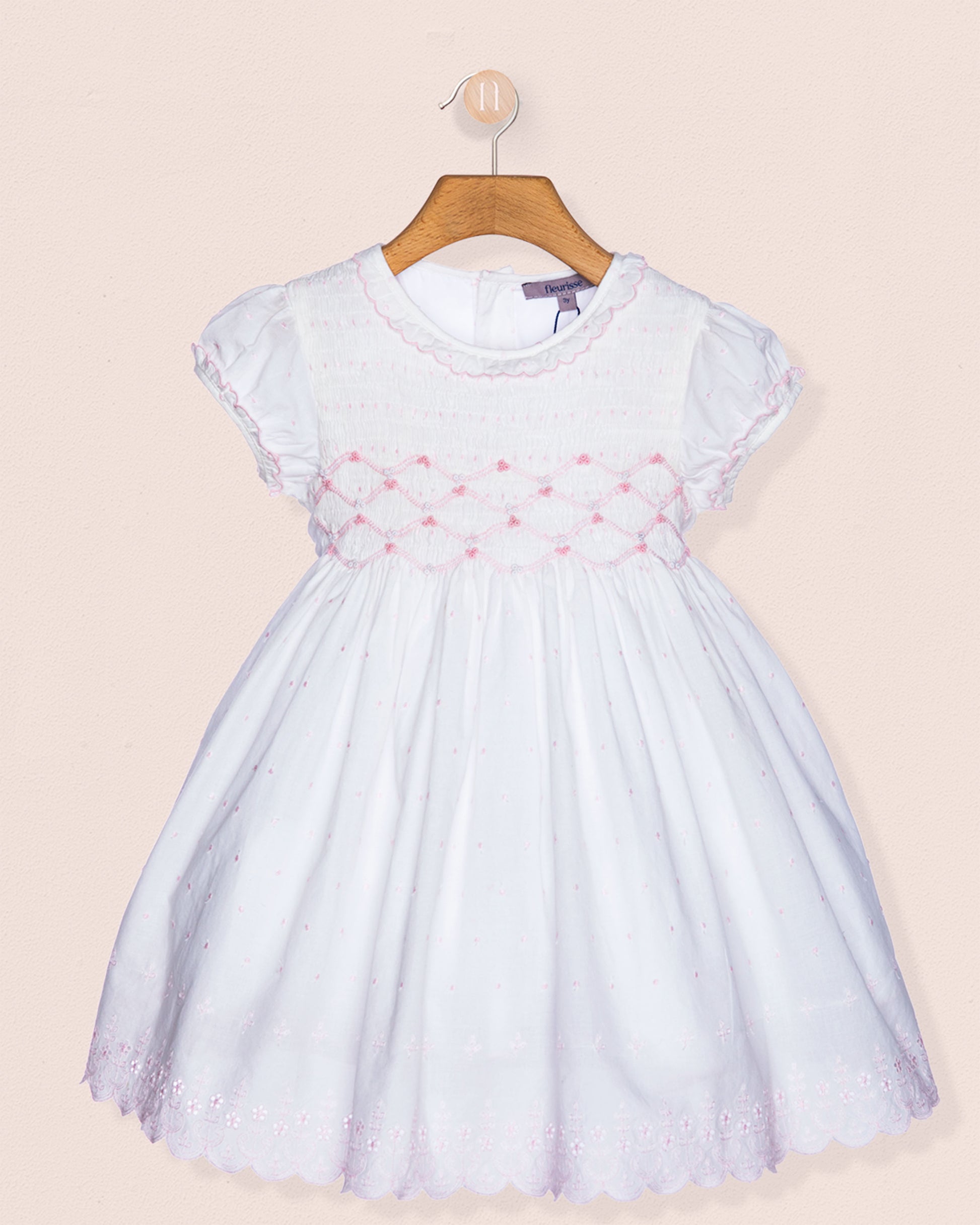 White dress with pink floral embroidery on a beige background