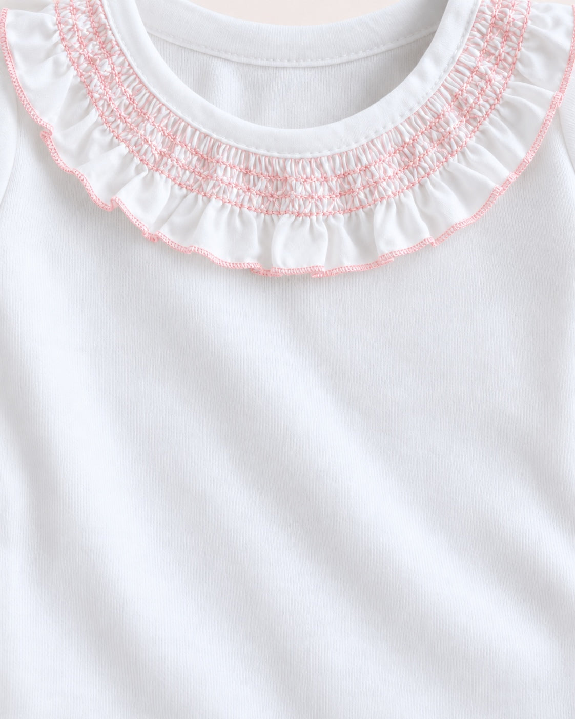 Close-up of a white garment with a ruffled collar featuring pink smocked stitching.
