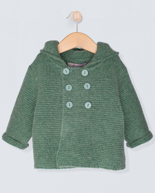 Green knitted jacket with buttons on a wooden hanger against a light gray background