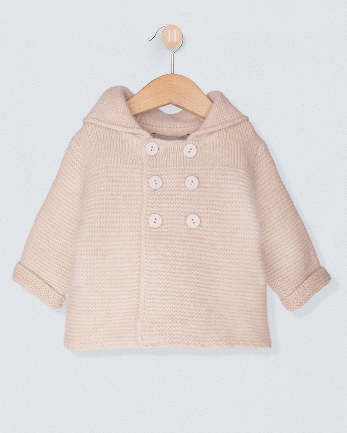 Beige baby coat on a wooden hanger against a light gray background