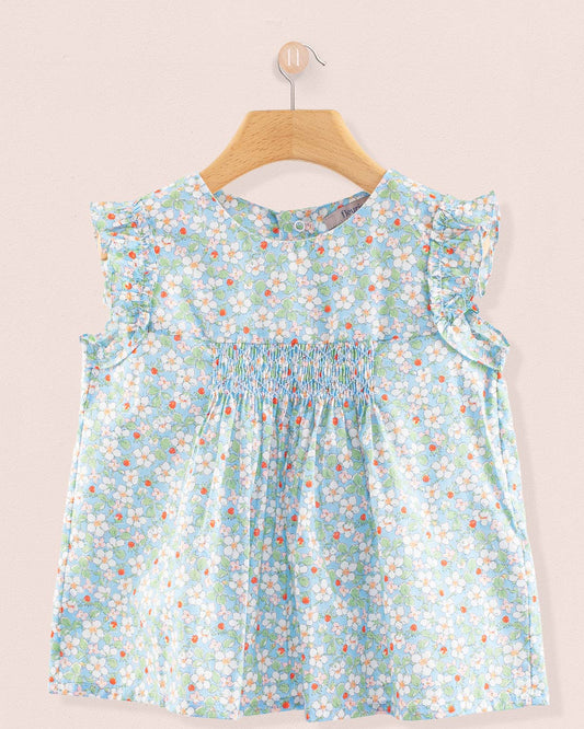 Front view of the Amelie Liberty Strawberry Field Blue Tunic, a sleeveless A-line top with hand-smocked detailing and ruffled sleeves in a pale blue floral Liberty print with white blossoms and small red strawberries.
