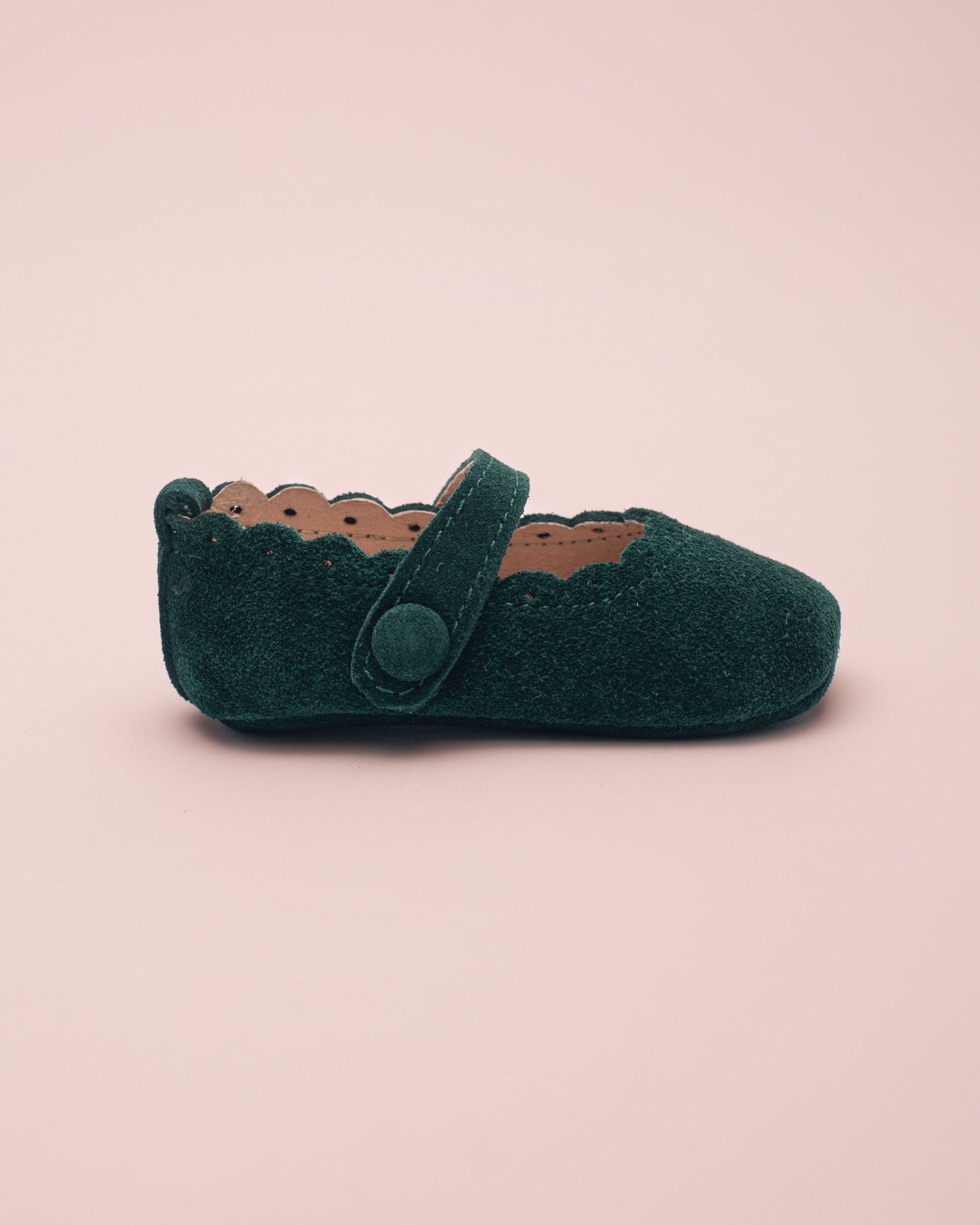 Green baby shoe with strap side view on a pink background