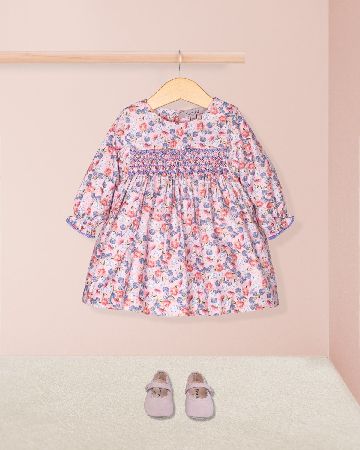 Floral dress on a hanger with matching shoes on the floor against a pink background