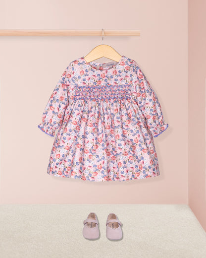 Floral dress on a hanger with matching shoes on the floor against a pink background