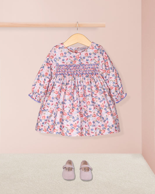 Floral dress on a hanger with matching shoes on the floor against a pink background