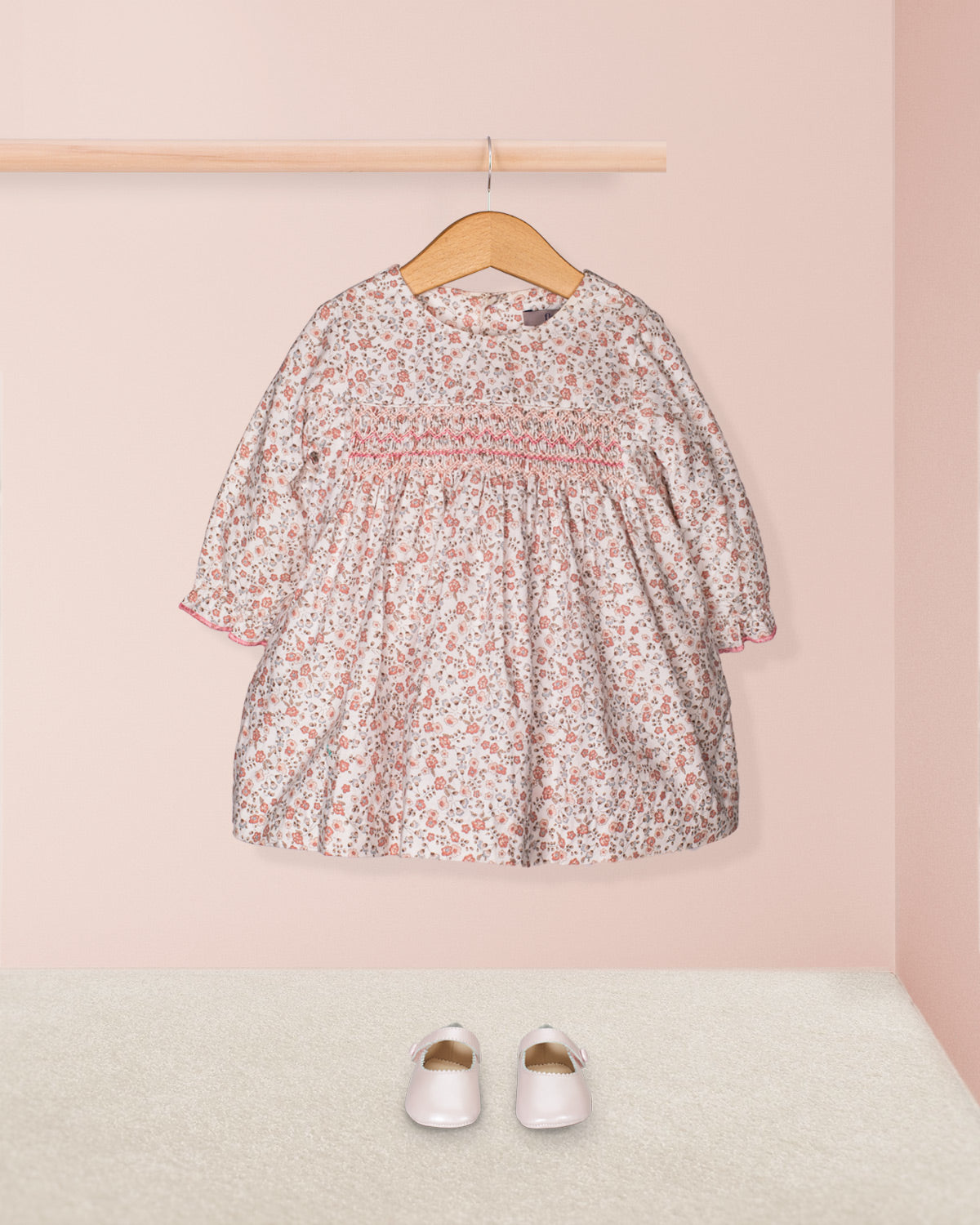 Floral dress on a hanger with white shoes on a pink background