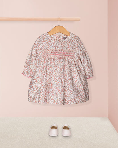 Floral dress on a hanger with white shoes on a pink background
