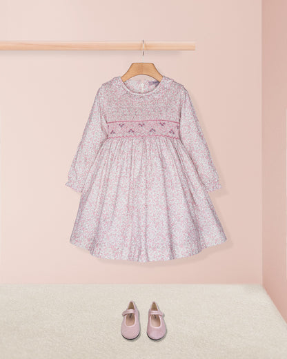 Pink floral dress on a hanger with pink shoes on the floor against a light pink wall.