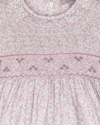 Close-up of a baby dress with floral pattern and smocked details, brand 'fleur' visible.