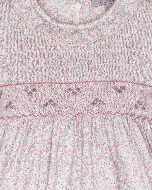 Close-up of a baby dress with floral pattern and smocked details, brand 'fleur' visible.