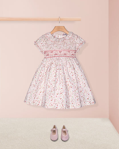 Floral dress on a hanger with pink shoes on the floor against a pink wall.