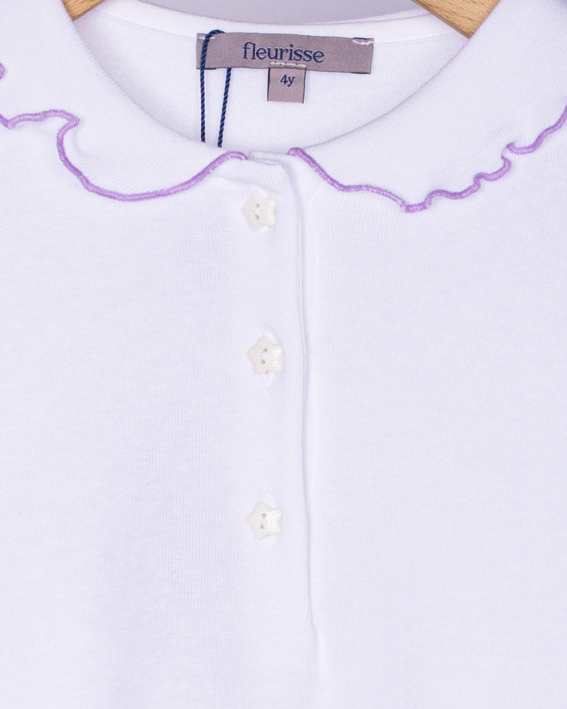 Close-up view of the soft brushed cotton fabric on the white long sleeve shirt, showing the delicate ruffle collar with lavender trim and three small white star-shaped buttons on the front placket.