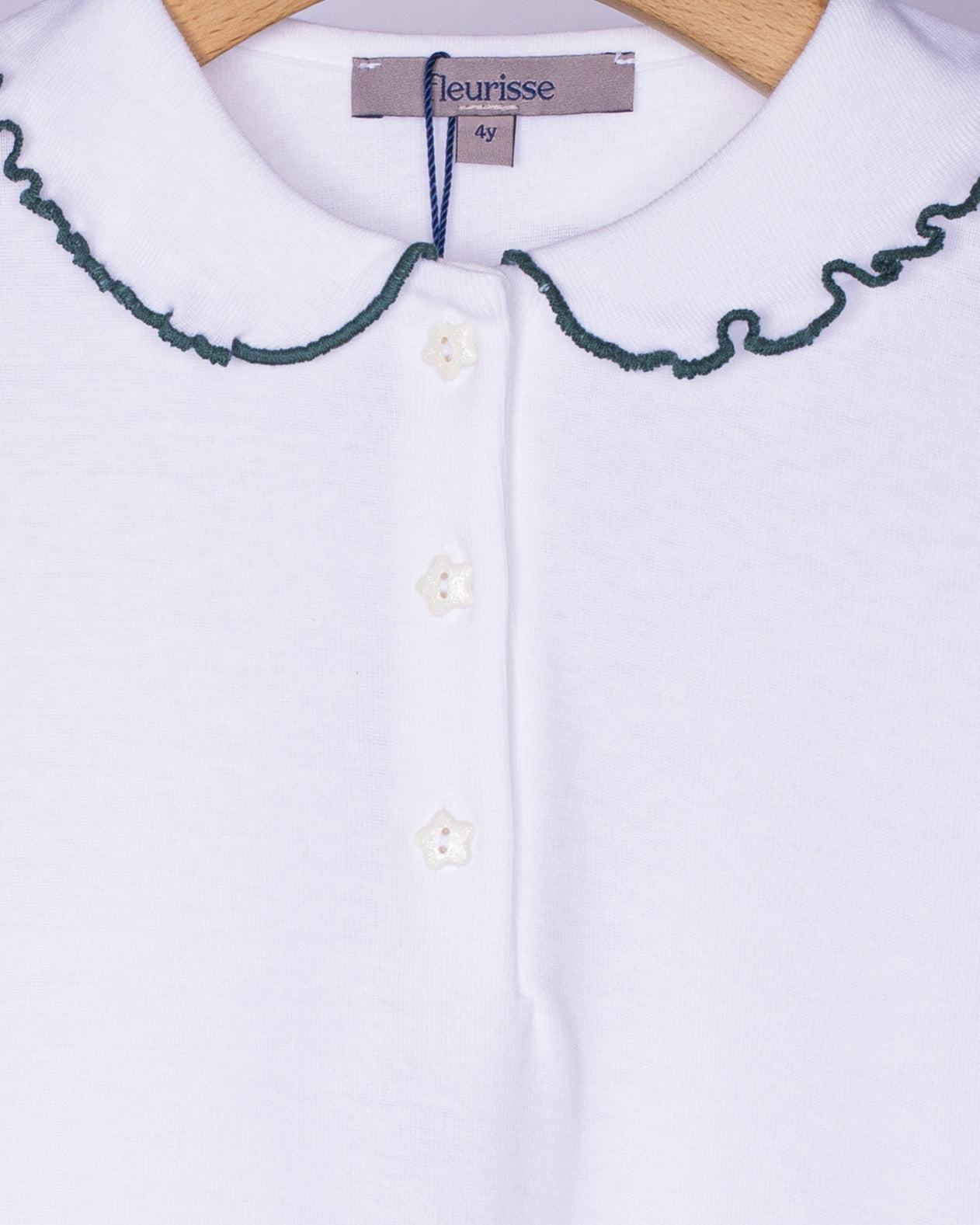 Close-up of white cotton blouse showing detailed pine green scalloped stitching along the rounded collar and white star-shaped buttons.