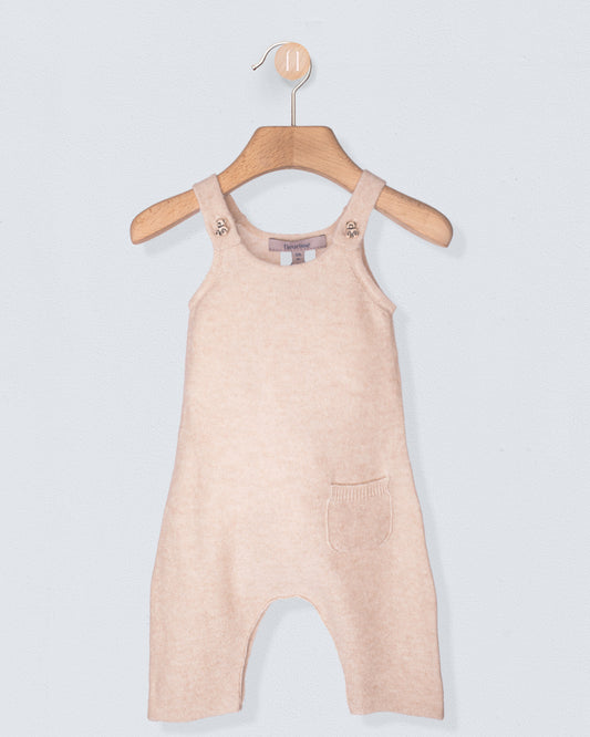 Beige cashmere overalls on a wooden hanger against a light gray background