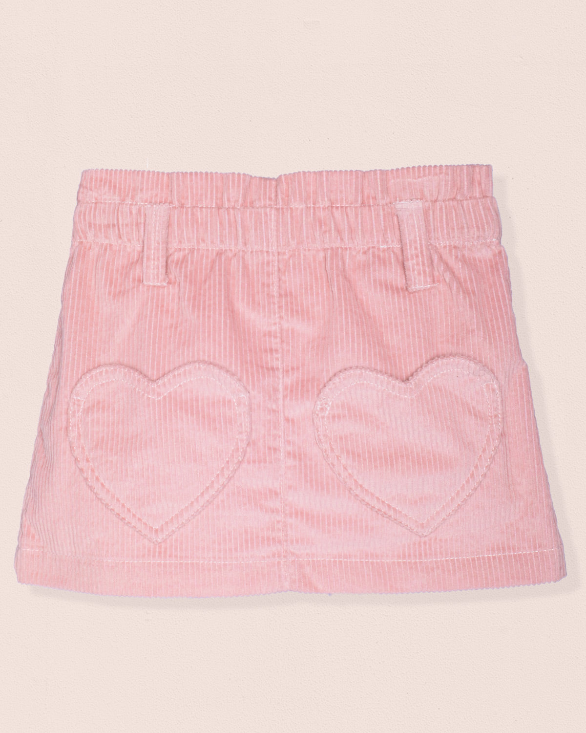 Pink corduroy skirt with heart shaped pockets on a light pink background