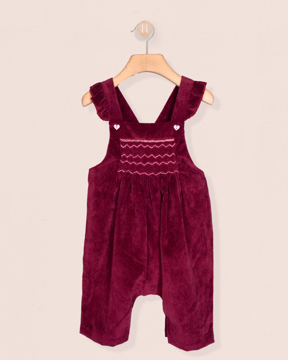 Burgundy velvet romper with ruffled straps on a beige background