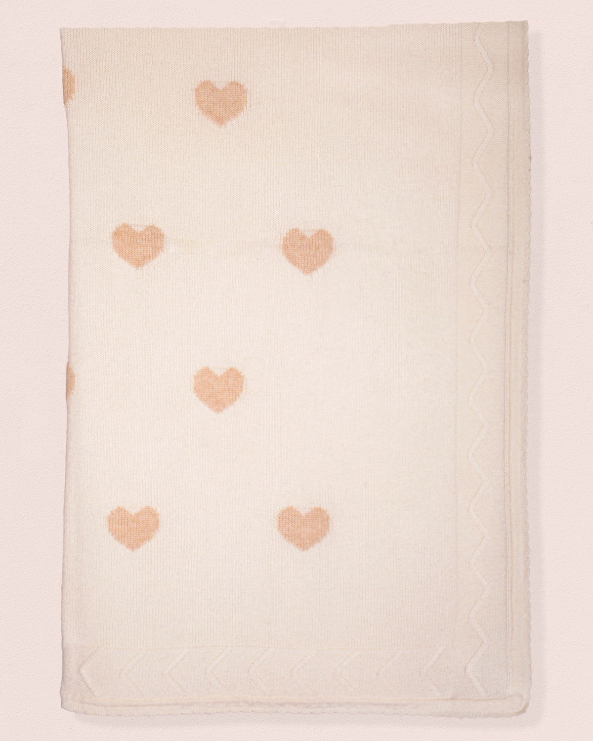 Beige blanket with pink heart patterns on a light pink background