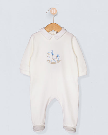Off-white baby footie made of soft Italian velour, with long sleeves and an embroidered blue rocking horse on the chest, hung on a wood hanger.