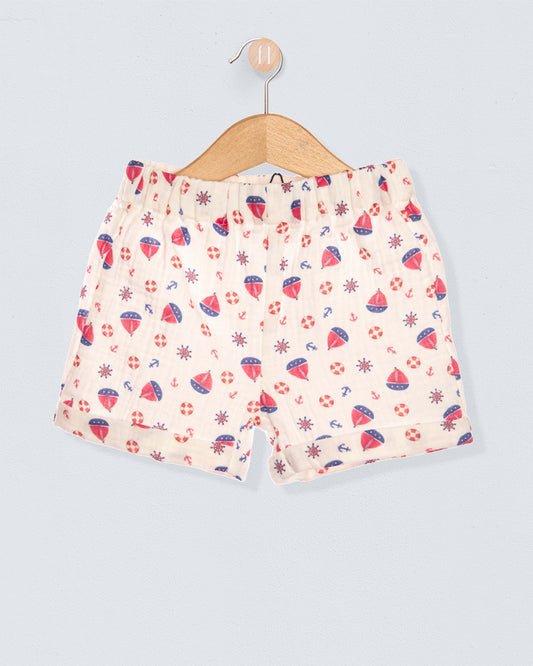 White shorts with red anchor and sailboat designs on a hanger against a light blue background.