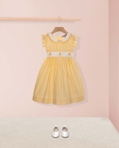 Yellow striped dress on a hanger against a pink wall with white shoes on the floor.