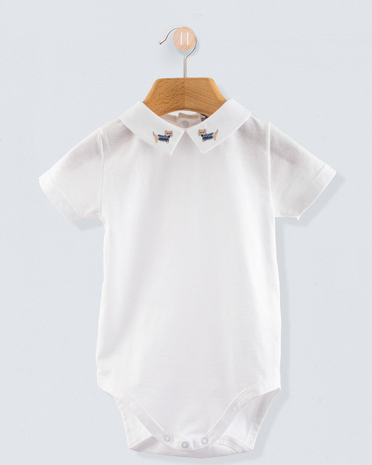 Front view of the Andreas Onesie with Embroidered Denim Dachshund, a short-sleeve white cotton jersey onesie with a crisp collar featuring embroidered dachshund dogs in denim blue sweaters.