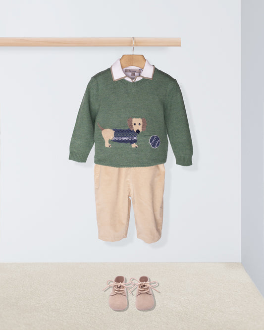 Children's outfit with green sweater and beige pants on a hanger, accompanied by shoes on the floor.
