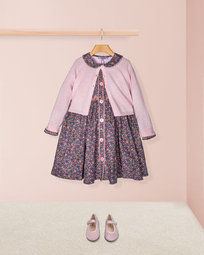 Pink cardigan over a floral dress with matching shoes on a pink background