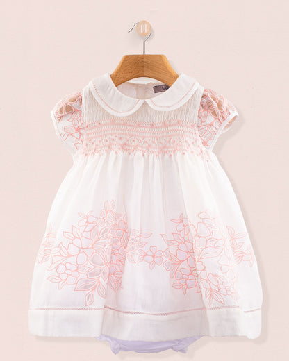 Front view of Baby Emmy Doppia Pink Smock Dress Set hanging on a wooden hanger showing pink hand smocking and floral embroidery on white cotton fabric