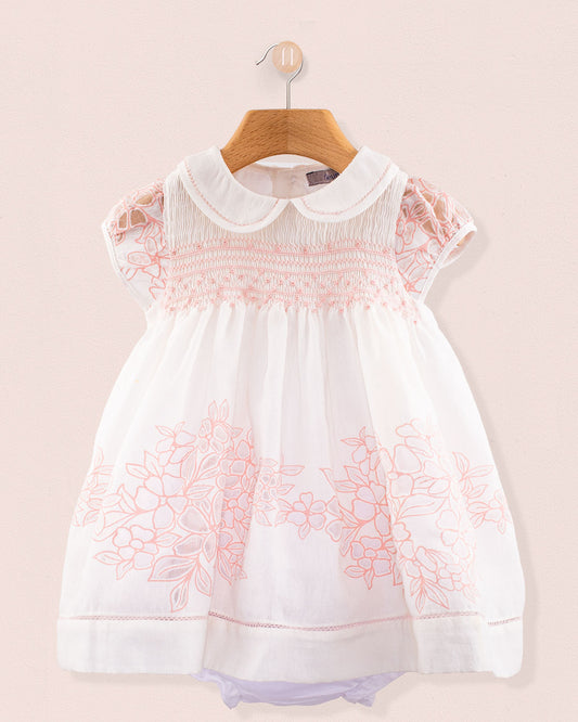 Front view of Baby Emmy Doppia Pink Smock Dress Set hanging on a wooden hanger showing pink hand smocking and floral embroidery on white cotton fabric