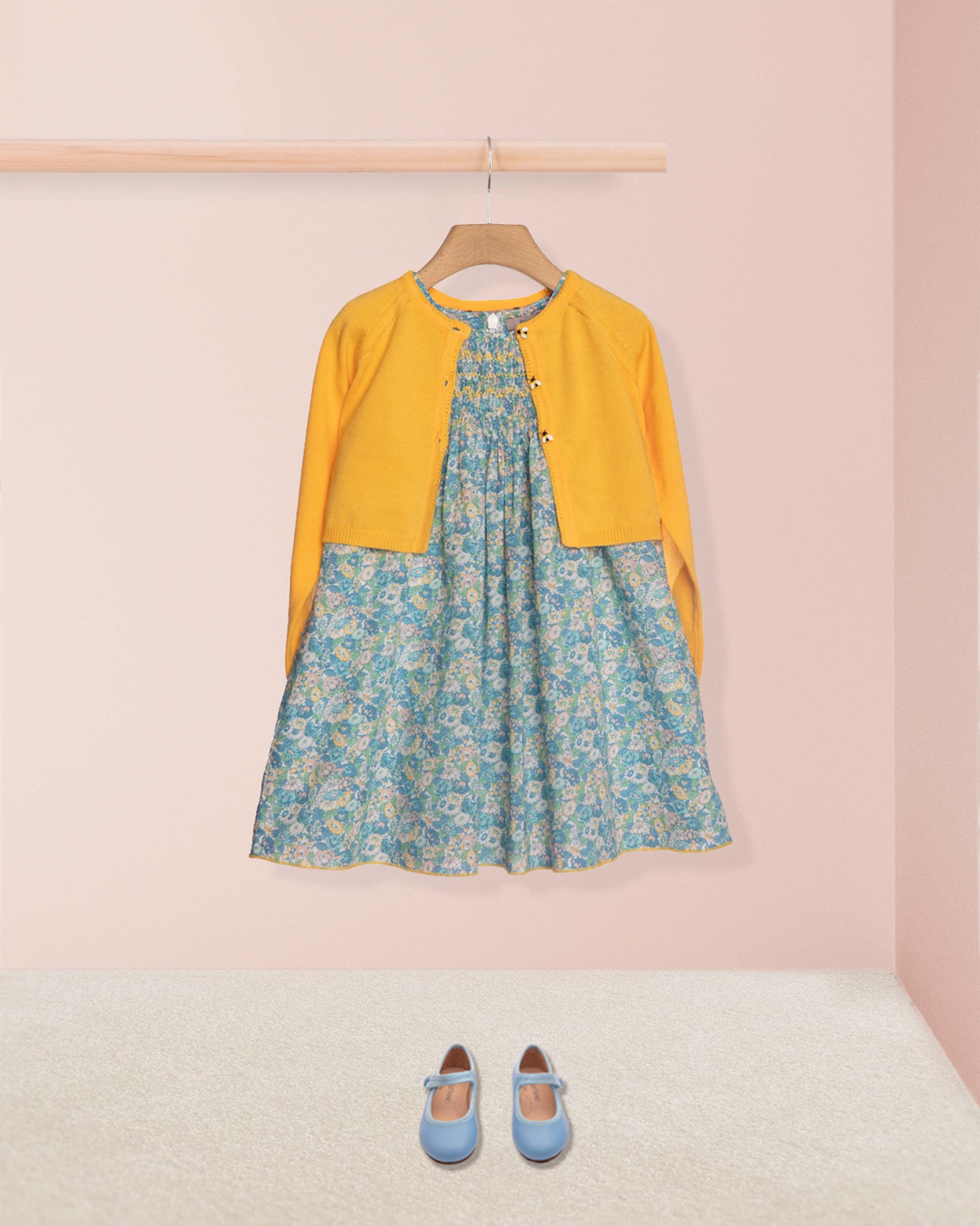 Floral dress with yellow cardigan and blue shoes on a pink background