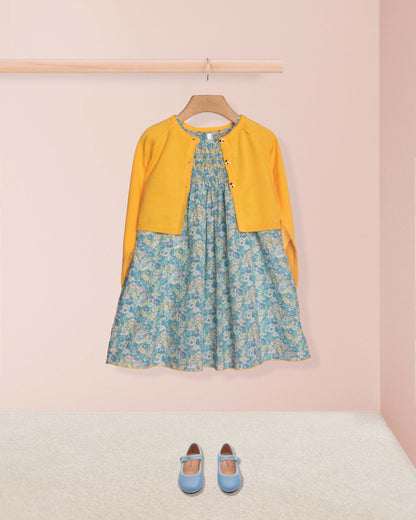 Floral dress with yellow cardigan and blue shoes on a pink background