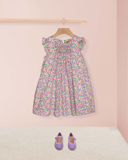 Floral dress on a hanger with matching shoes on the floor against a pink wall.