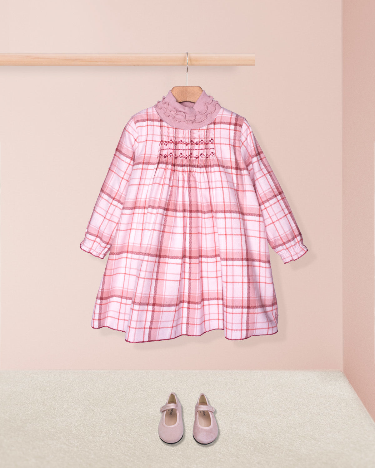 Pink plaid dress on a hanger with matching shoes on the floor against a pink background