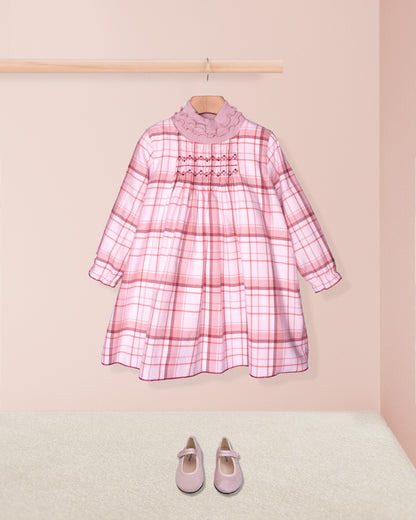 Pink plaid dress on a hanger with matching shoes on the floor against a pink background