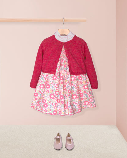 Children's outfit with floral dress and red cardigan on a pink background