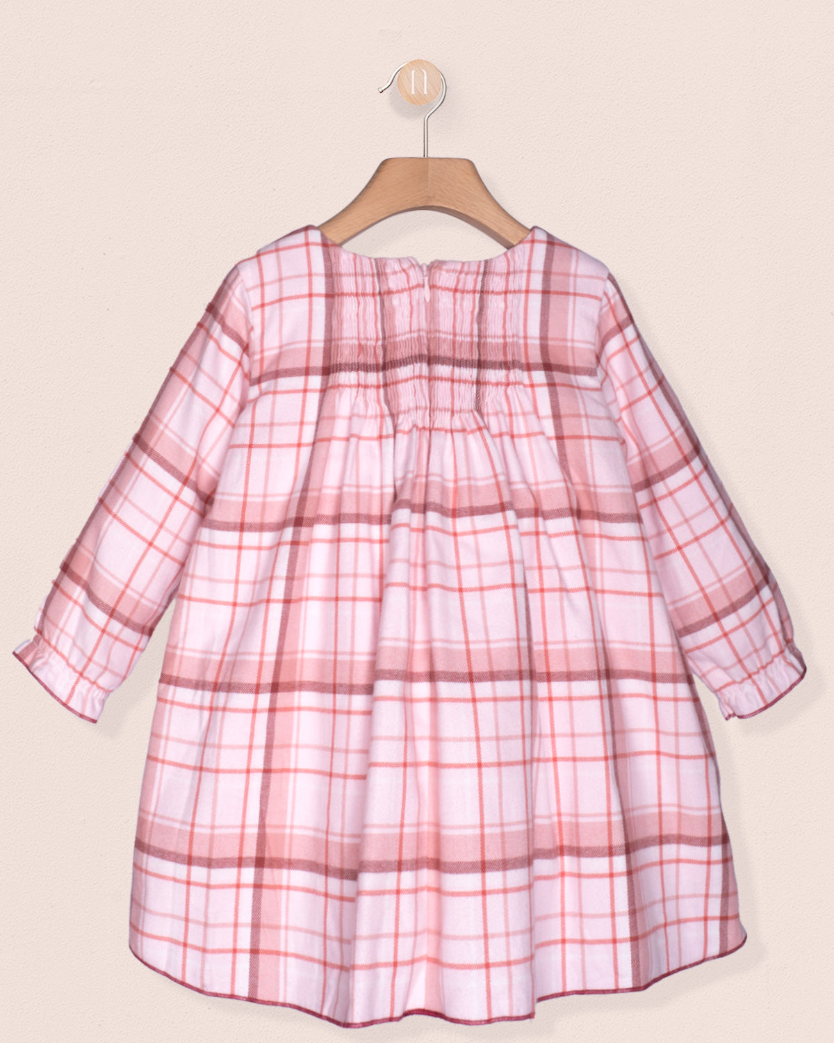 Pink plaid dress on a hanger against a beige background