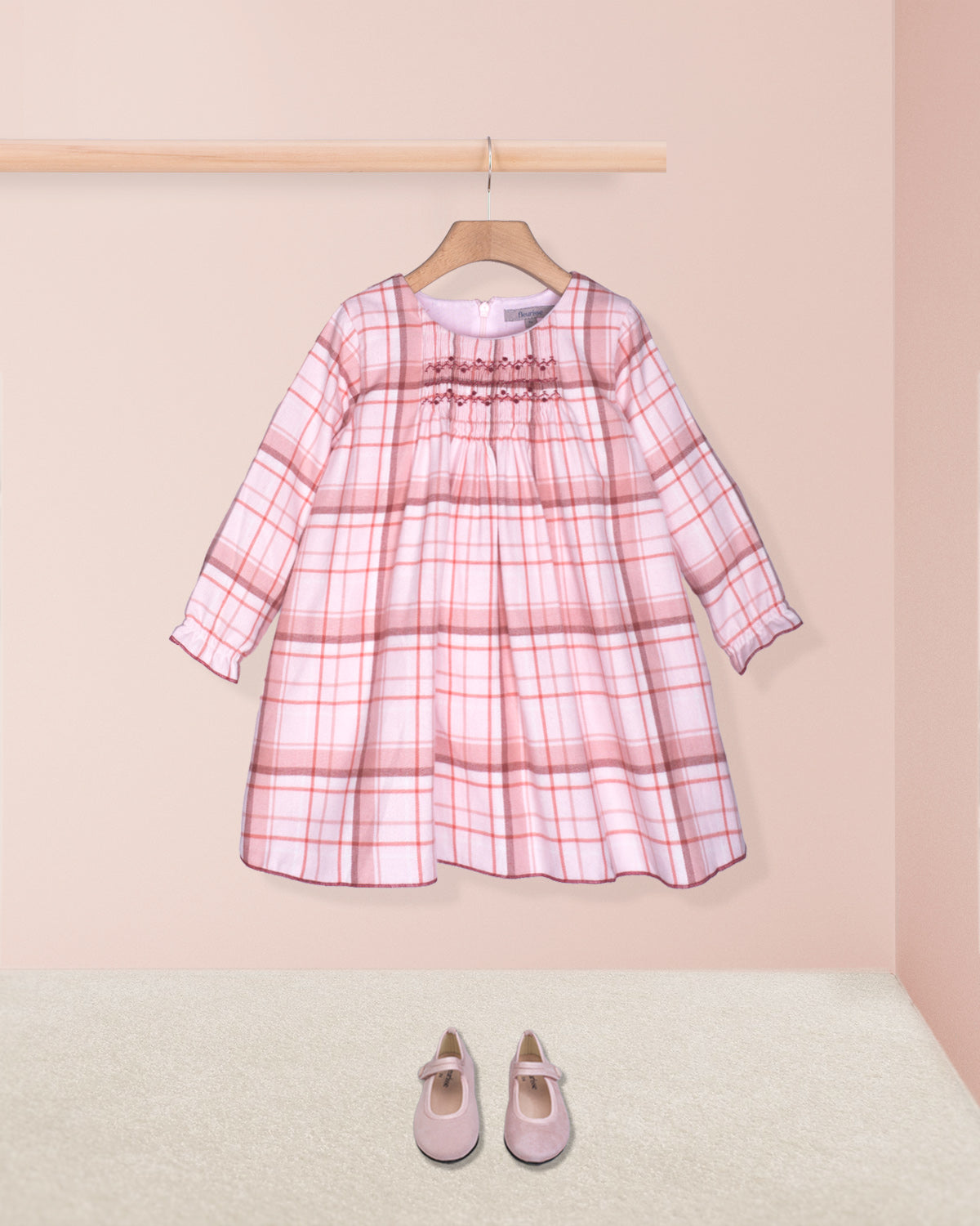 Pink plaid dress on a hanger with matching shoes on the floor against a pink background