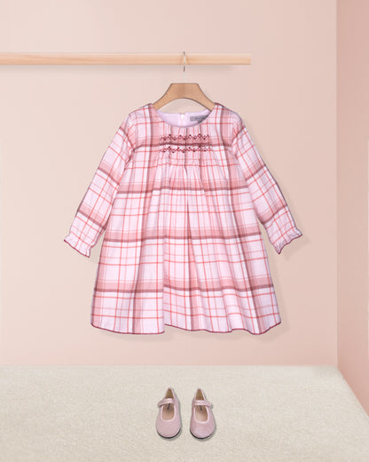 Pink plaid dress on a hanger with matching shoes on the floor against a pink background