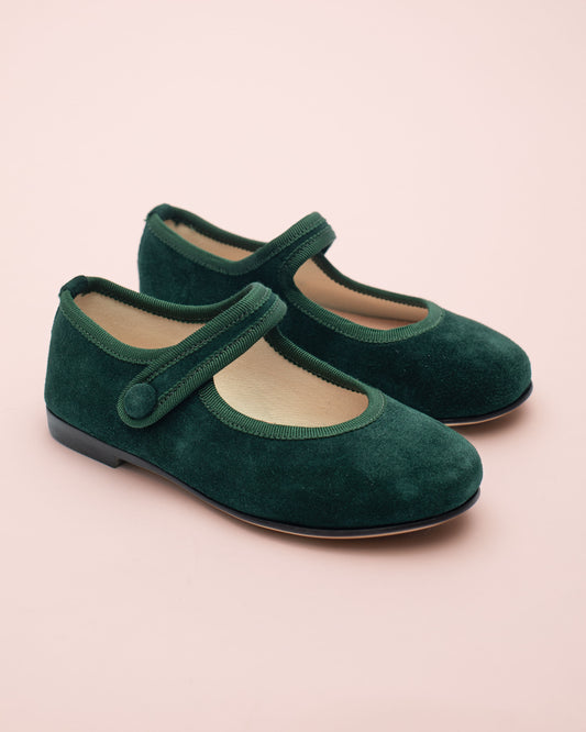 Pair of green suede shoes with a strap on a light pink background