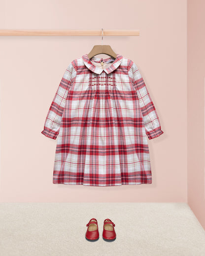 Red and white checkered dress on a hanger with matching shoes on the floor against a pink wall.