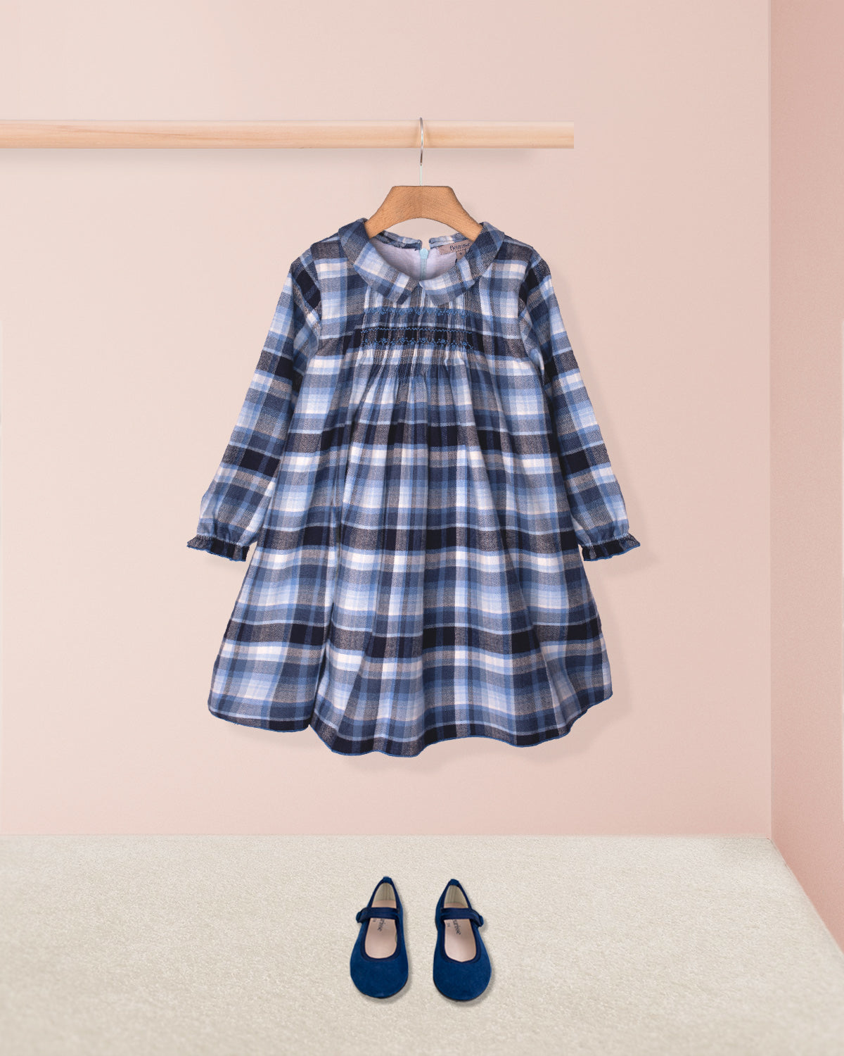 Blue plaid dress on a hanger with matching shoes on the floor against a pink wall.