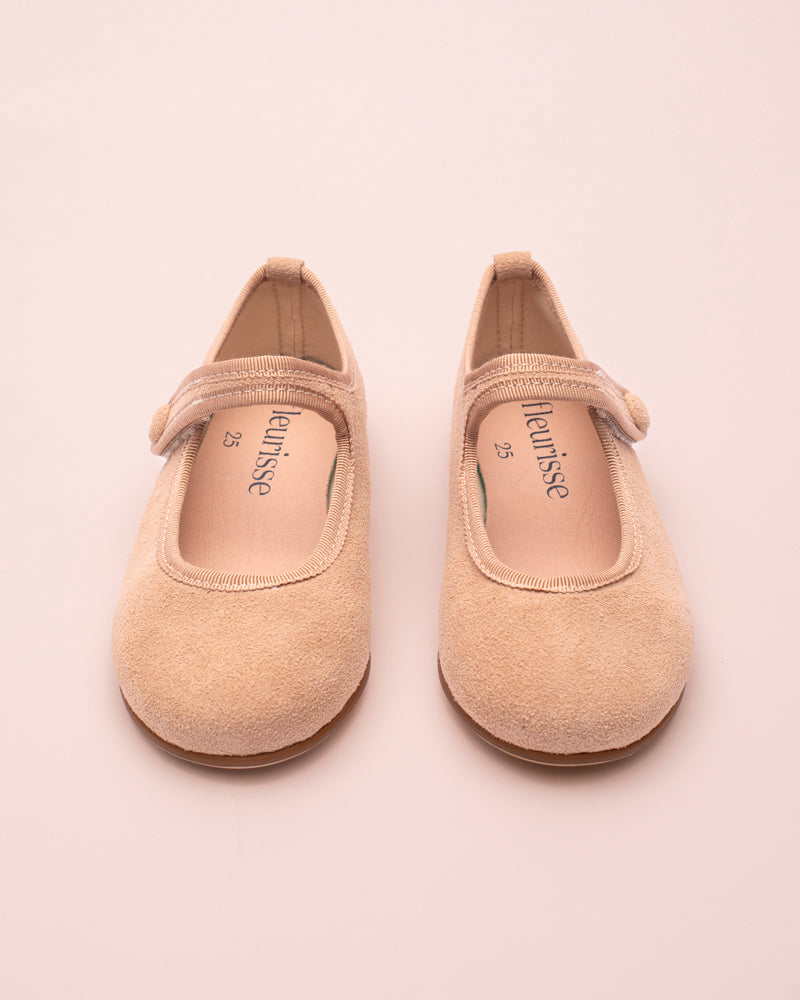 Pair of beige suede children's shoes with on a light pink background