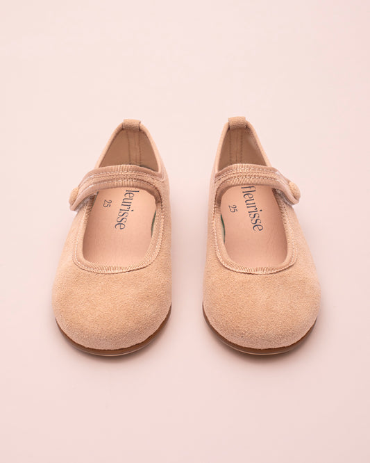 Pair of beige suede children's shoes with on a light pink background