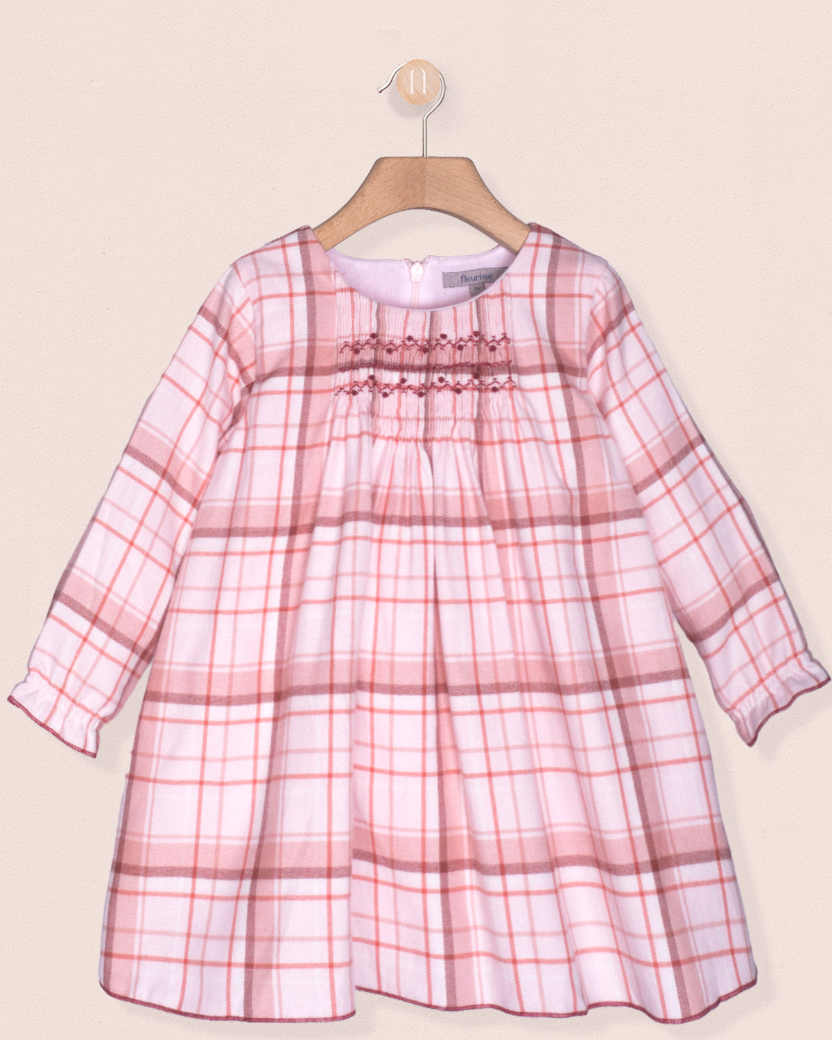 Pink and white checkered dress on a hanger against a beige background