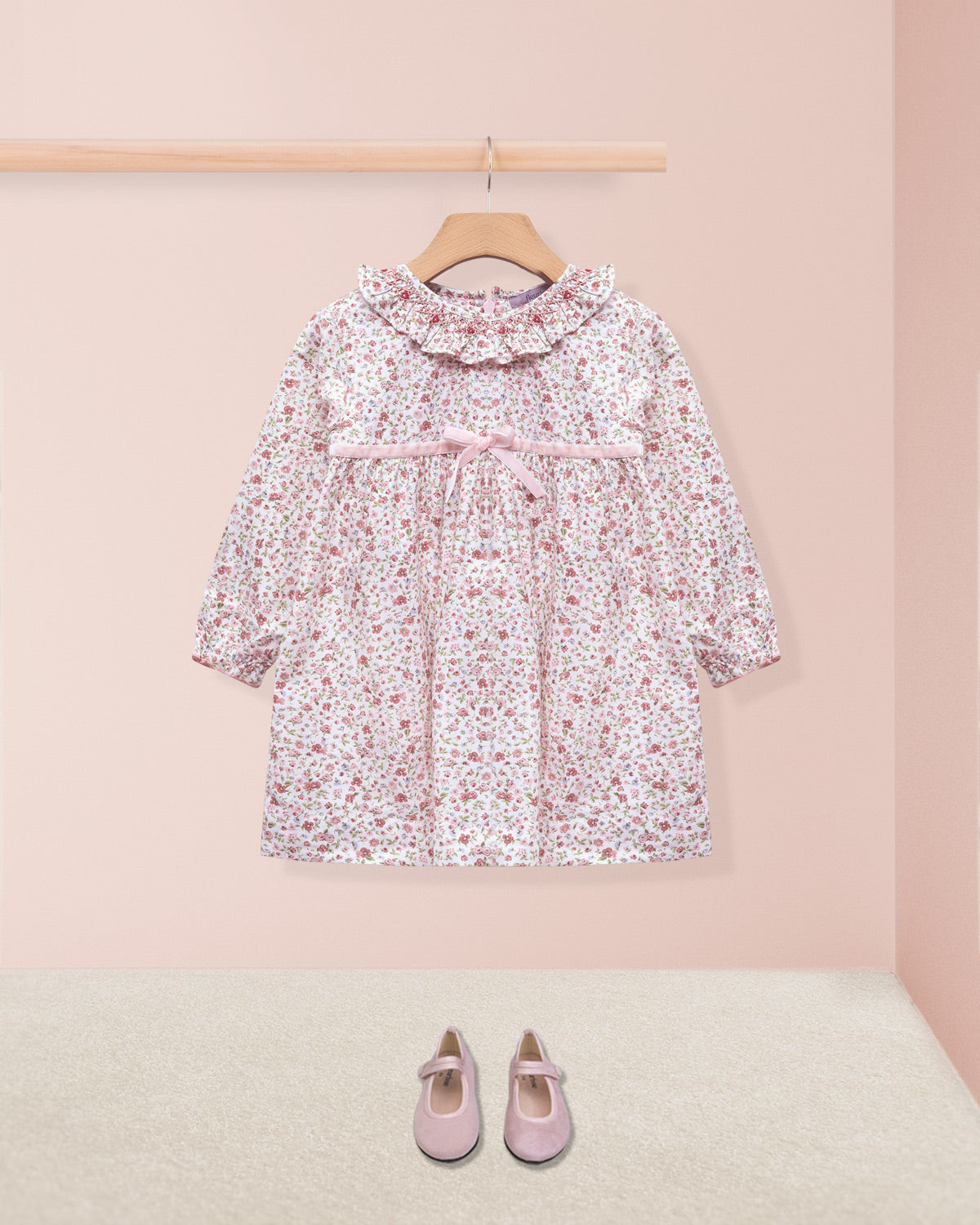 Floral dress on a hanger with pink shoes on the floor against a pink wall